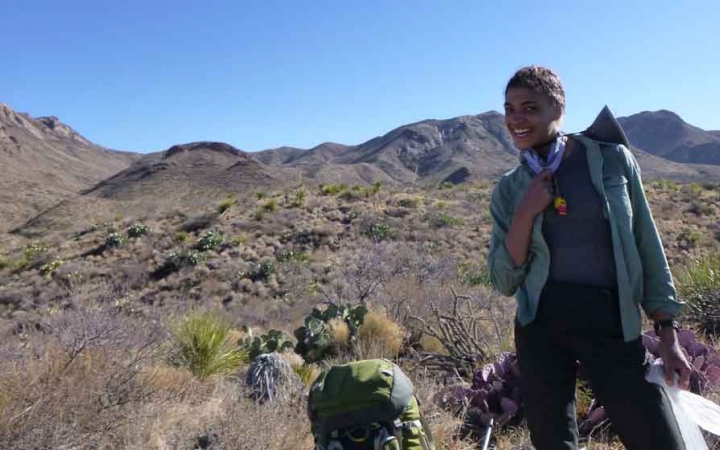 a student smiles at the camera in front of a desert landscape